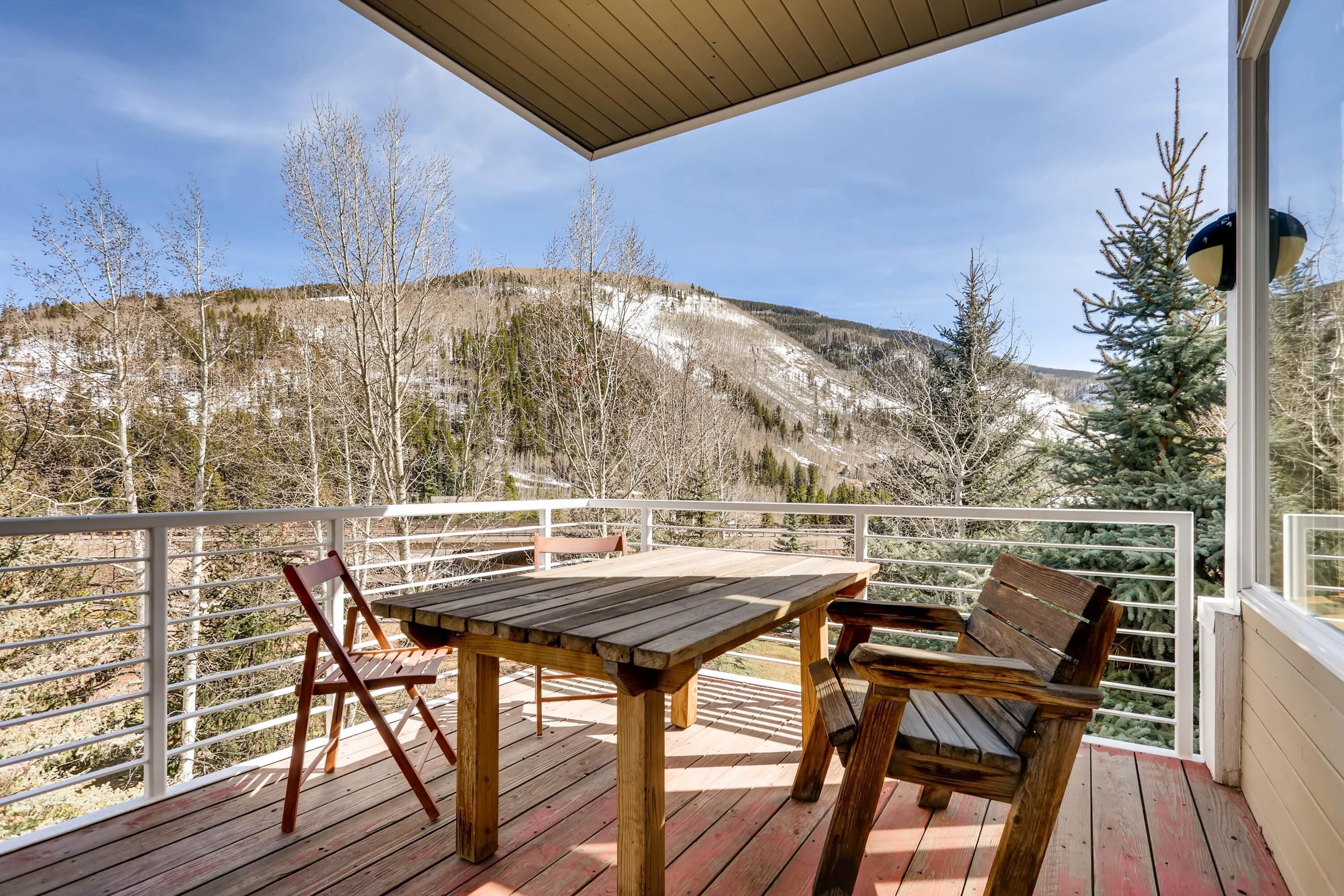 A wooden deck with a table and chairs, overlooking a mountainous landscape.