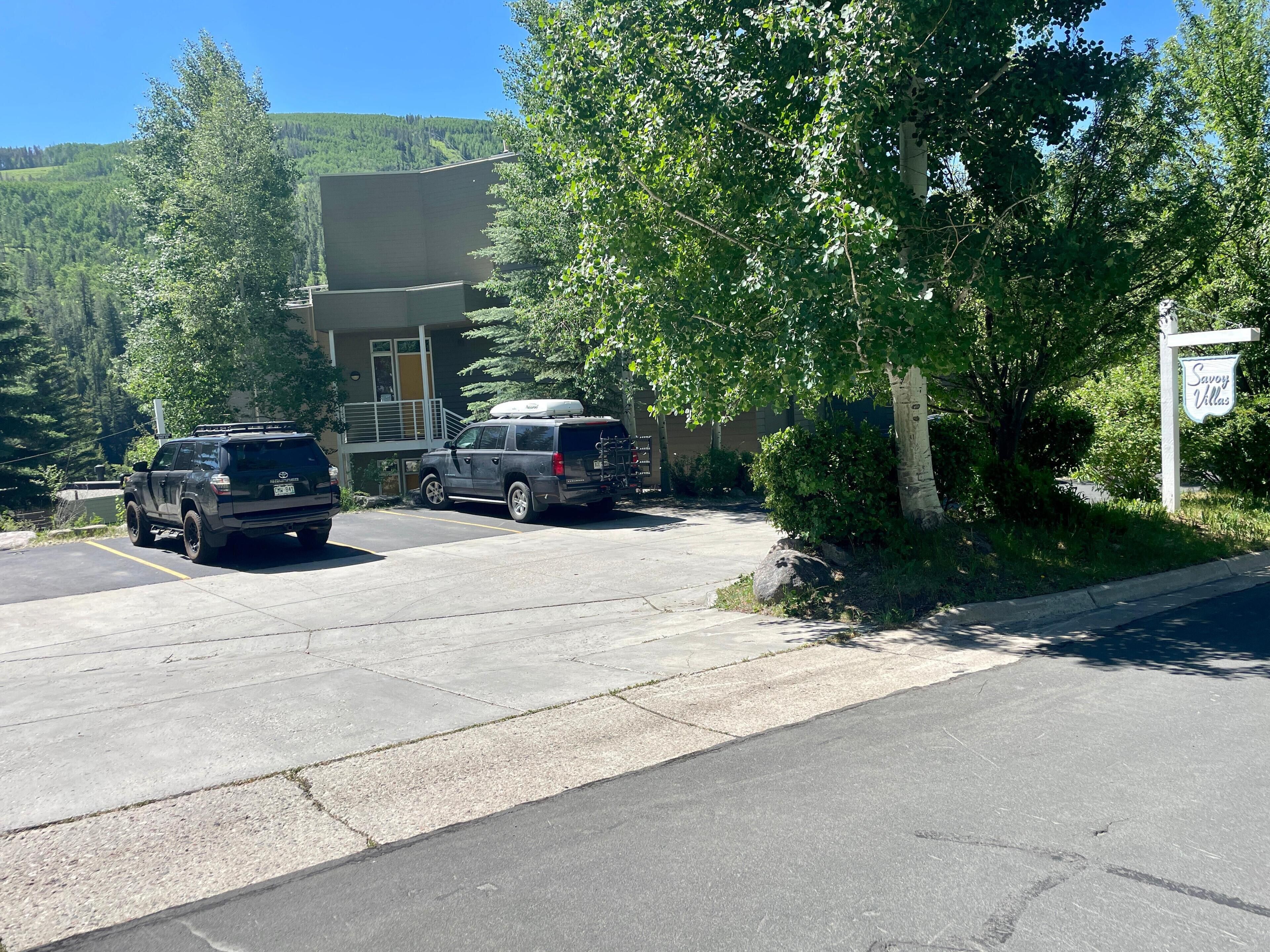 Un parcheggio con due SUV, un edificio con un balcone e un cartello con la scritta 'Savoy Villas'.
