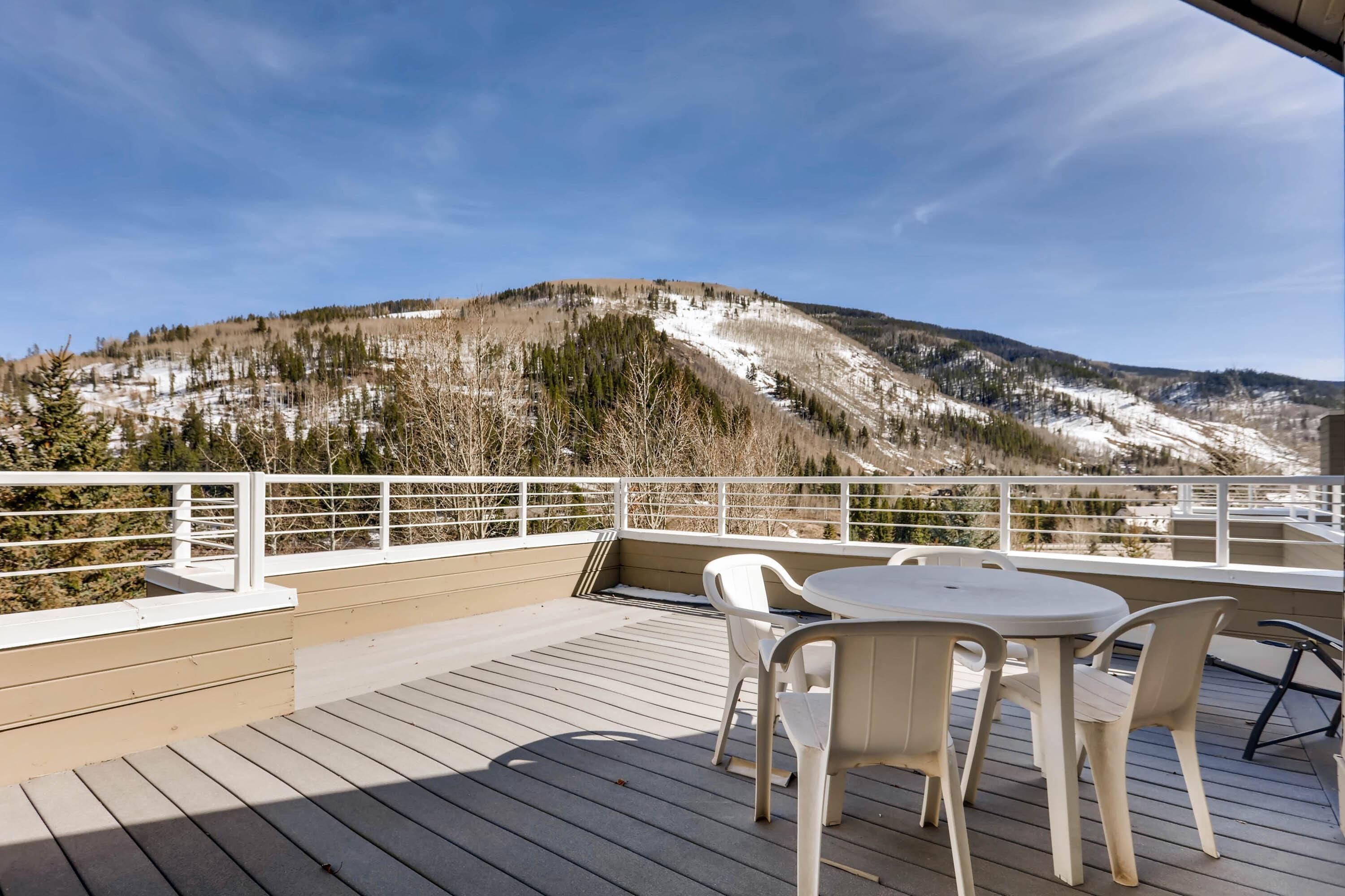 A deck with a table and chairs, overlooking a snowy mountain landscape.