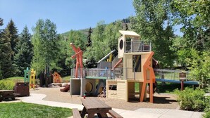 Une aire de jeux avec un toboggan, des structures d’escalade et une table de pique-nique.