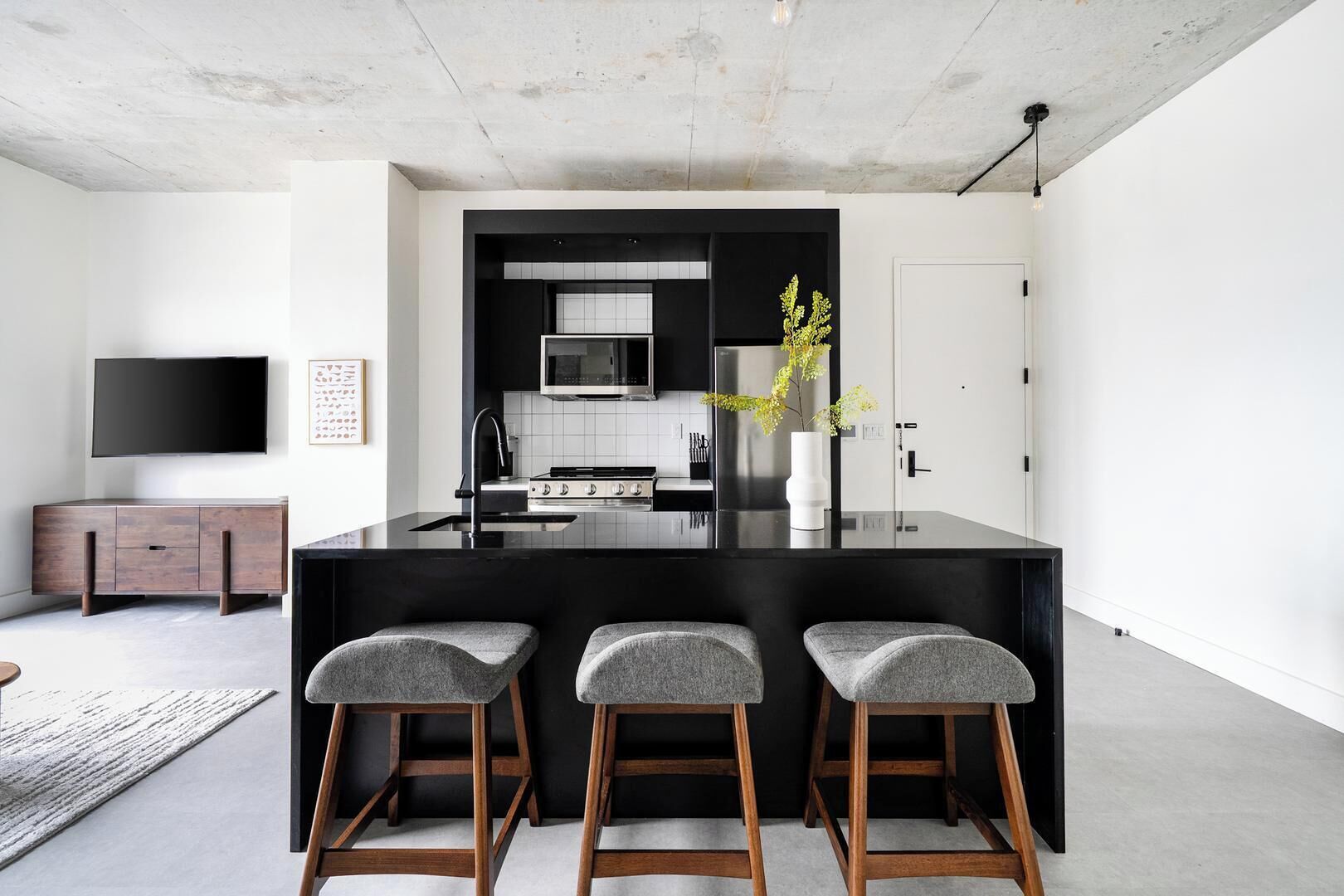 A modern kitchen with a central island, bar stools, a flat-screen TV, and a minimalist design.