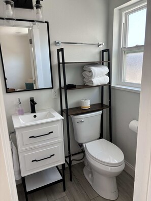 Ein kleines Badezimmer mit Waschbecken, Toilette, Spiegel und Ablagefläche mit Handtüchern.