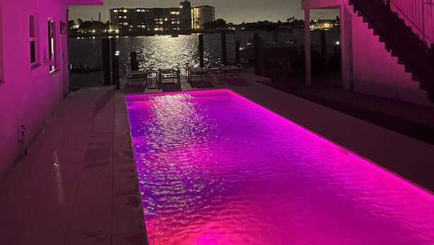 Ein Pool mit rosarotem Licht, eine Treppe und Blick auf die nächtliche Stadt.