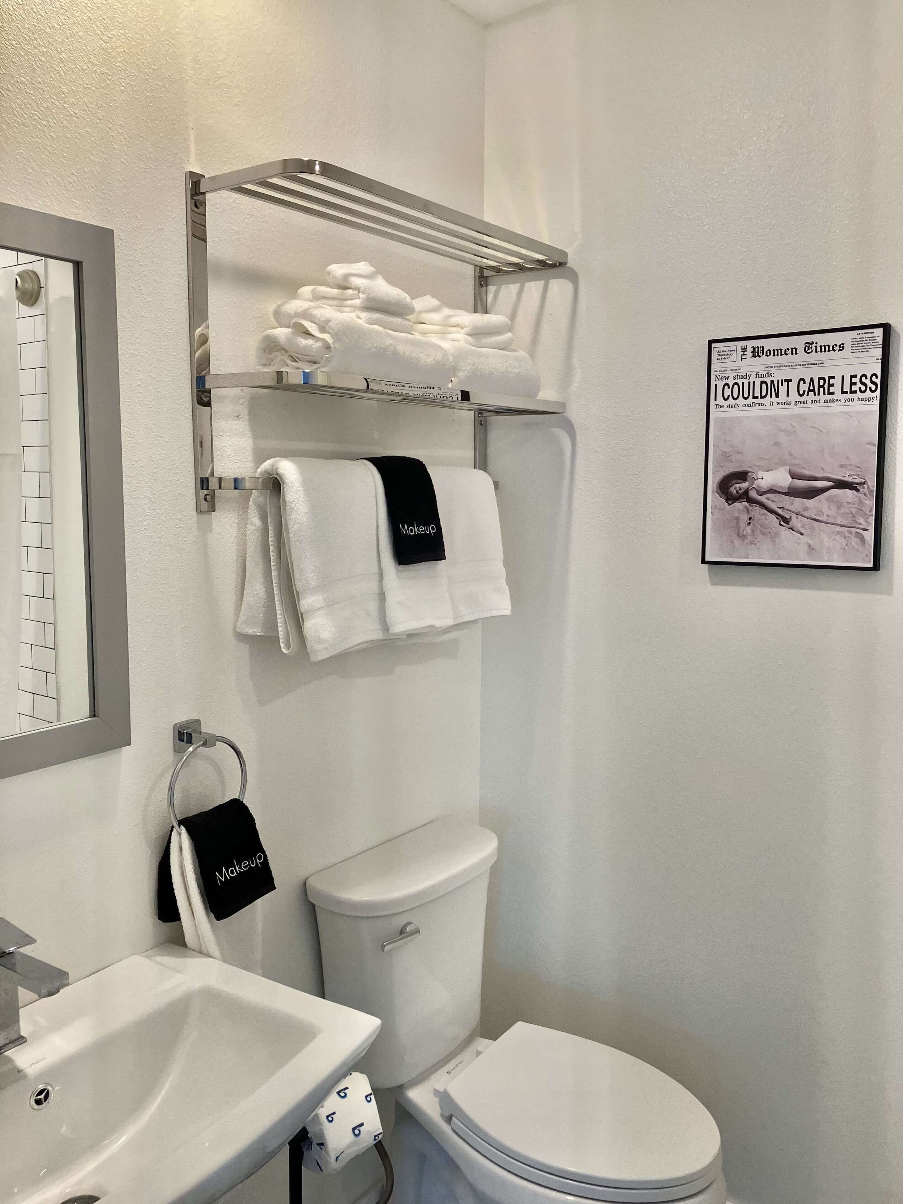 Une salle de bain avec un lavabo, des toilettes et un porte-serviettes, le tout de couleur blanche. Un journal encadré est accroché au mur.