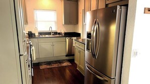 Una cocina con electrodomésticos de acero inoxidable, armarios de colores claros y piso de madera.