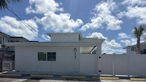Un edificio blanco con el número '617' en la fachada, una cerca blanca y una palmera al fondo.