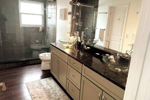 Ein modernes Badezimmer mit einer Duschkabine, einer Toilette und einem Waschtisch mit großem Spiegel und zwei Glasvasen.