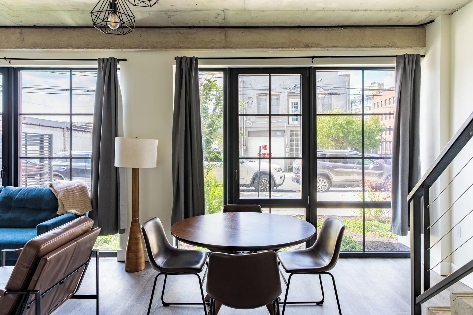A room with a sofa, a table with chairs, a lamp, and large windows with curtains.