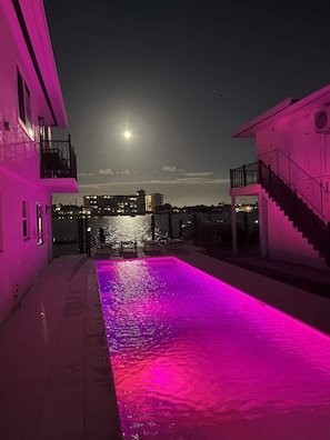 Une piscine éclairée de lumières roses, un escalier et une vue sur la ville la nuit.