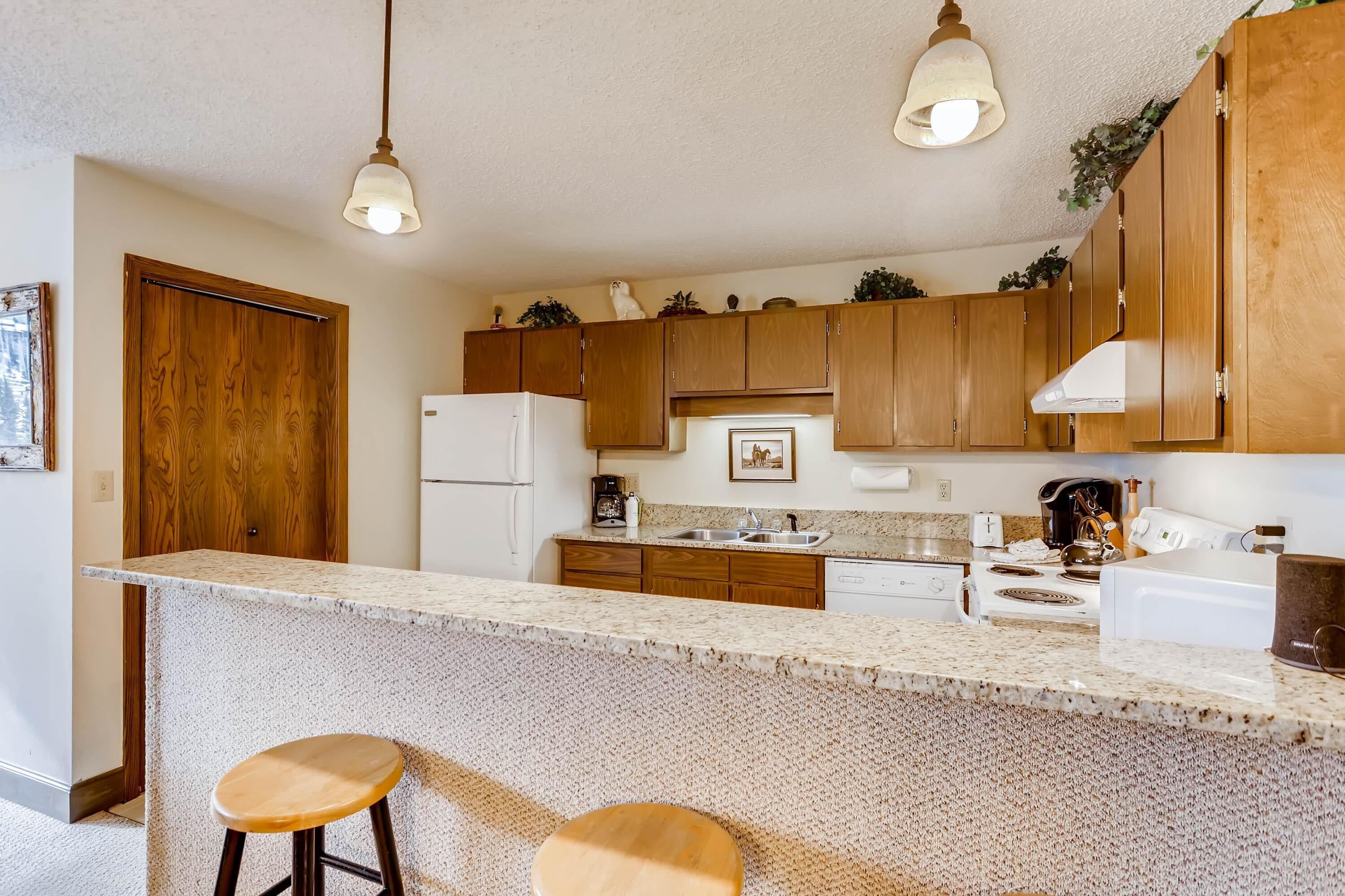 Una cocina con armarios de madera, encimera de granito y dos taburetes de bar.