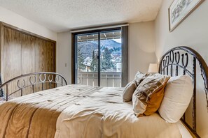 A bedroom with a bed, a window with a view of mountains, a door, and a metal headboard. - Scorpio 304, 2BD Vail Condo With Wood Fireplace (Vail)