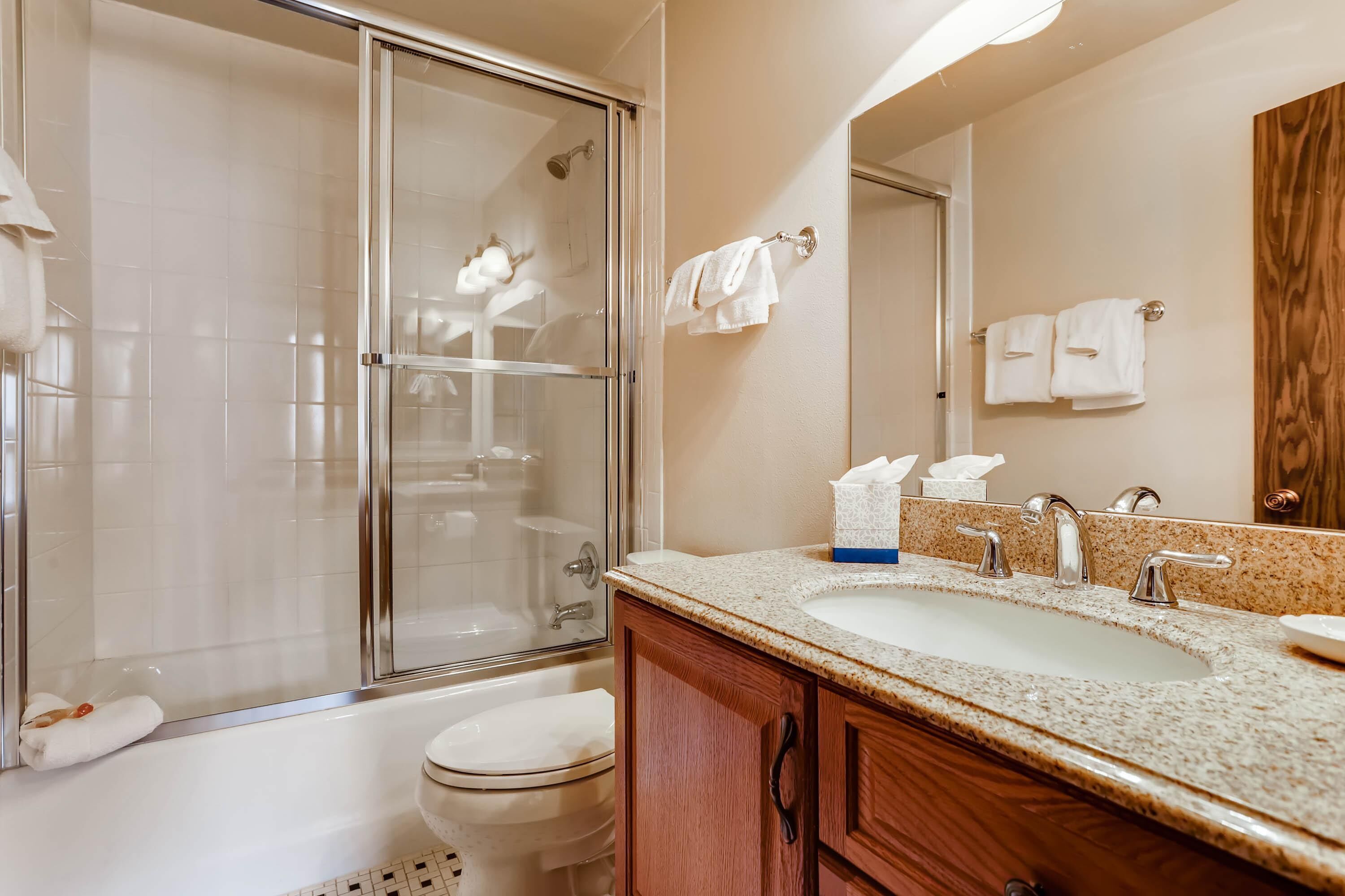 Ein Badezimmer mit Glasdusche, Waschbecken mit Spiegel und Toilette.
