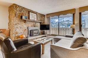 Ein Wohnzimmer mit Steinwand, Kamin, Flachbildfernseher, Sofa und einem Balkon mit Aussicht.