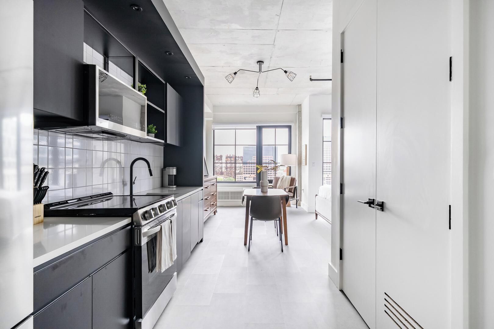 A modern kitchen with a stove, sink, and cabinets, leading to a dining area with a table and chairs.