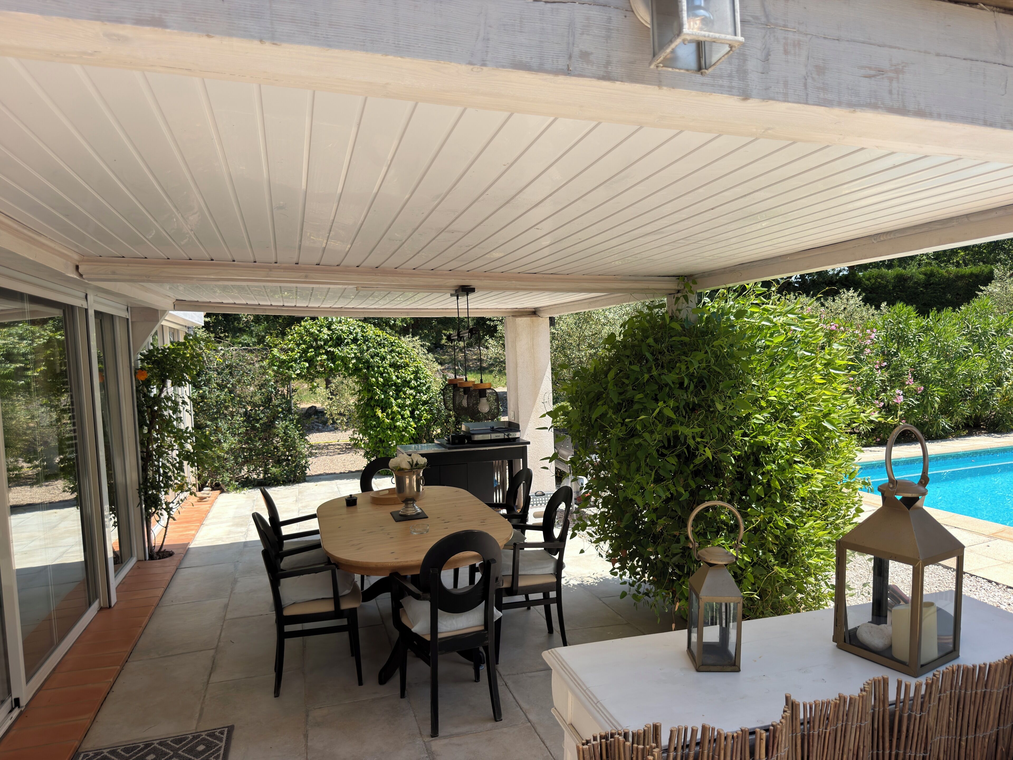 An outdoor patio with a table and chairs, a lantern, and a pool in the background.