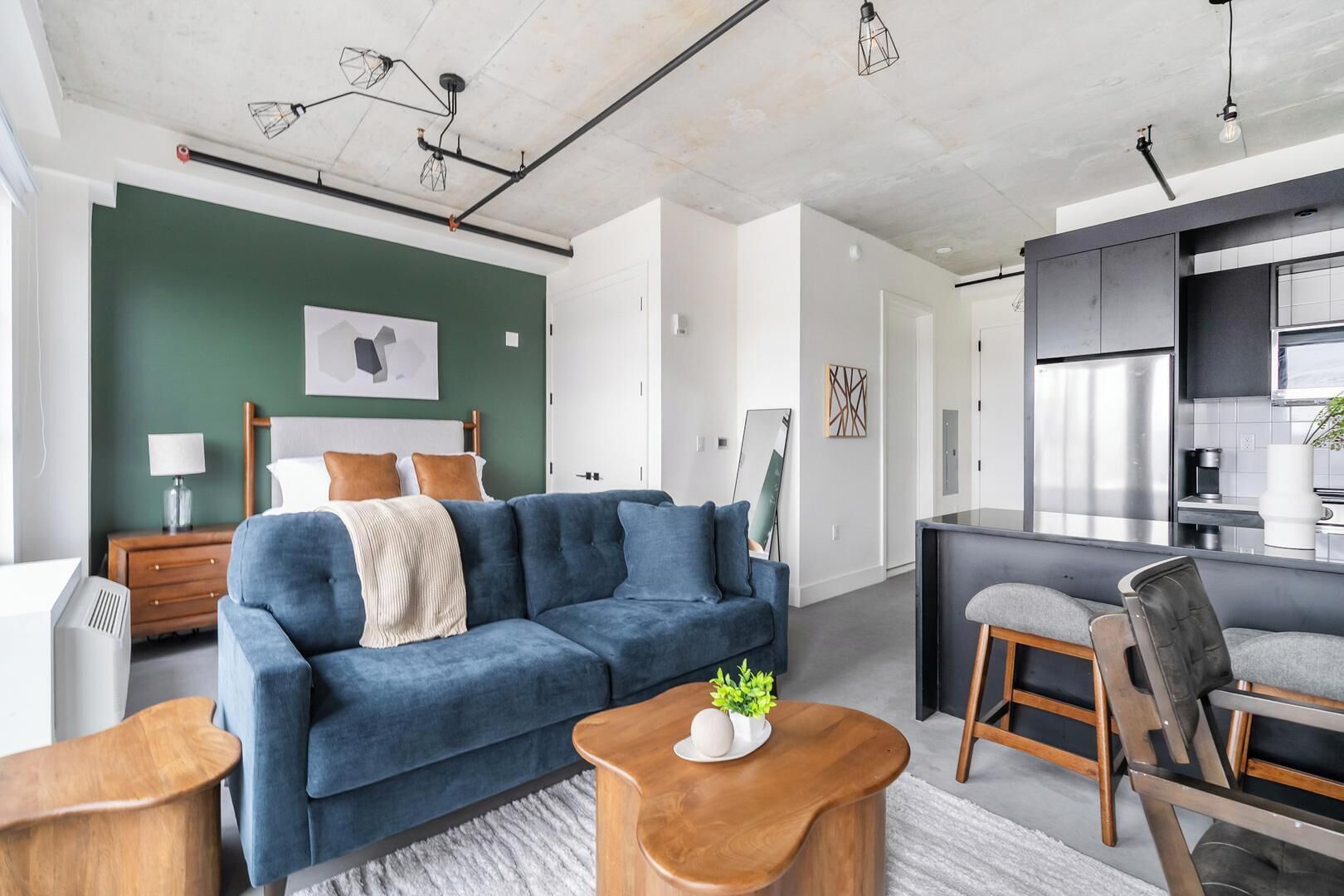 Una sala de estar moderna con un sofá azul, una mesa de centro de madera y una cocina con refrigerador y armarios.