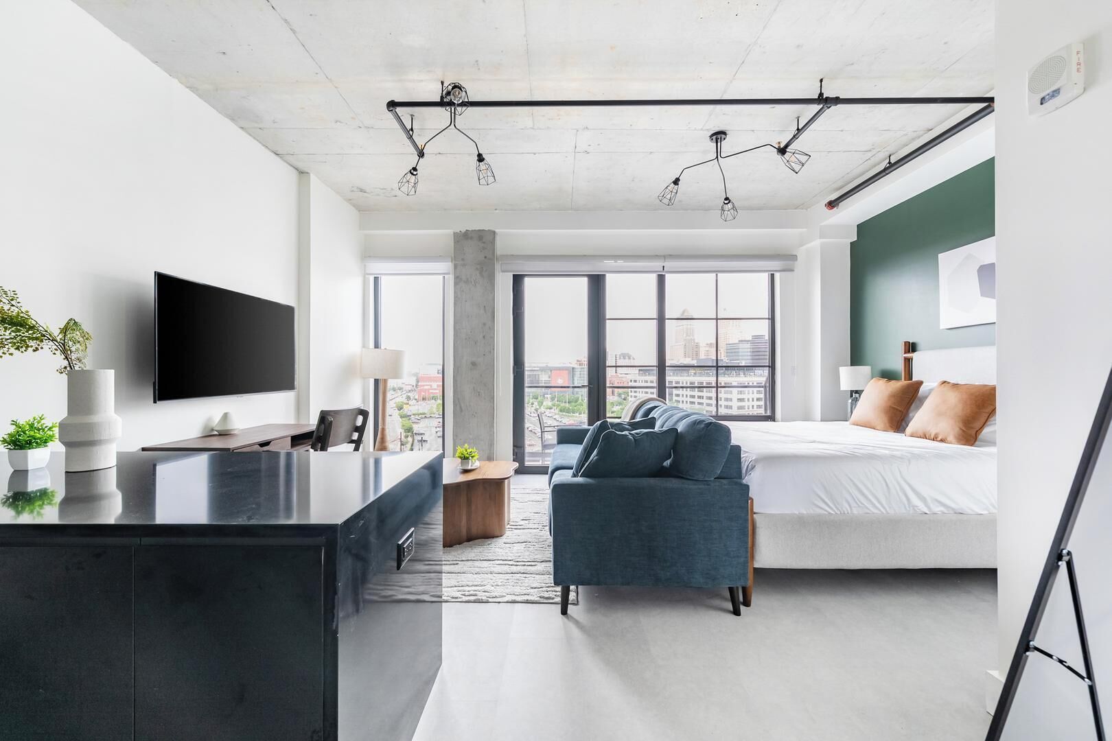 A modern hotel room with a large bed, a desk, a TV, and a view of the city.