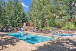 A swimming pool with lounge chairs, surrounded by trees and a stone wall. - Sun Vail 11b, 3BD Condo (Vail)