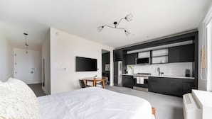 Ett modernt hotellrum med en stor säng, ett matbord, ett litet kök och en tv som är monterad på väggen.