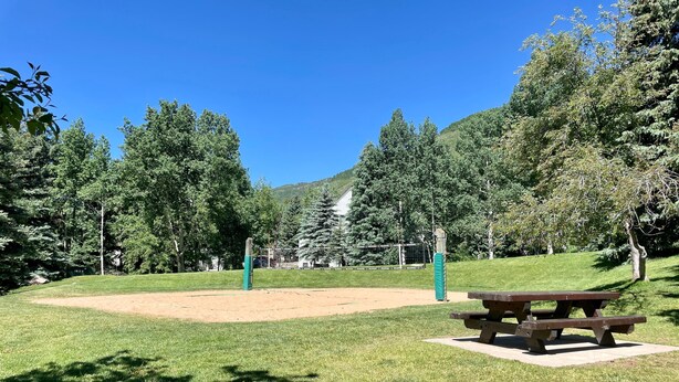 A park with a volleyball net, picnic table, and surrounding greenery. - Sun Vail 22b, 2BD Condo With Vail Mountain Views (Vail)