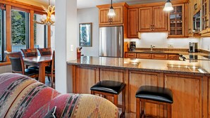 A modern kitchen with wooden cabinets, stainless steel appliances, and a large island with bar stools. - Sun Vail 22b, 2BD Condo With Vail Mountain Views (Vail)