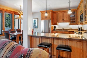 A modern kitchen with wooden cabinets, stainless steel appliances, and a large island with bar stools. - Sun Vail 22b, 2BD Condo With Vail Mountain Views (Vail)