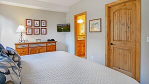 A bedroom with a bed, dresser, wall-mounted TV, wooden door, and framed pictures. - Sun Vail 22b, 2BD Condo With Vail Mountain Views (Vail)