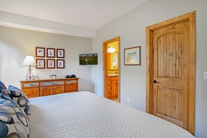 A bedroom with a bed, dresser, wall-mounted TV, wooden door, and framed pictures. - Sun Vail 22b, 2BD Condo With Vail Mountain Views (Vail)
