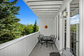 A covered balcony with a table and chairs, a glass door, and a view of trees and mountains. - Sun Vail 22b, 2BD Condo With Vail Mountain Views (Vail)