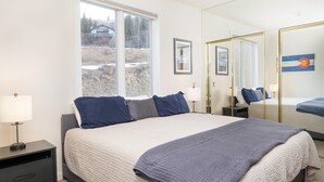 A bedroom with a large bed, bedside tables, a window, and a mirror. - Sun Vail 34b, 3BD Condo With Vail Mountain Views (Vail)