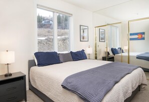 A bedroom with a large bed, bedside tables, a window, and a mirror. - Sun Vail 34b, 3BD Condo With Vail Mountain Views (Vail)