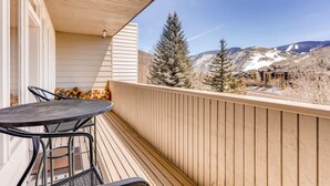 A balcony with a view of snow-capped mountains, a wooden railing, and a metal table with chairs. - Sun Vail 34b, 3BD Condo With Vail Mountain Views (Vail)