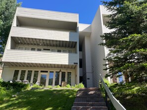 A multi-story building with a flat roof, a front entrance with steps, and a small garden area with grass and plants. - Sun Vail 34b, 3BD Condo With Vail Mountain Views (Vail)