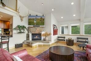 A spacious living room with a fireplace, a mounted deer head, a television, and a large window. - Tyrolean 5, 3BD Condo in Vail Village (Vail)