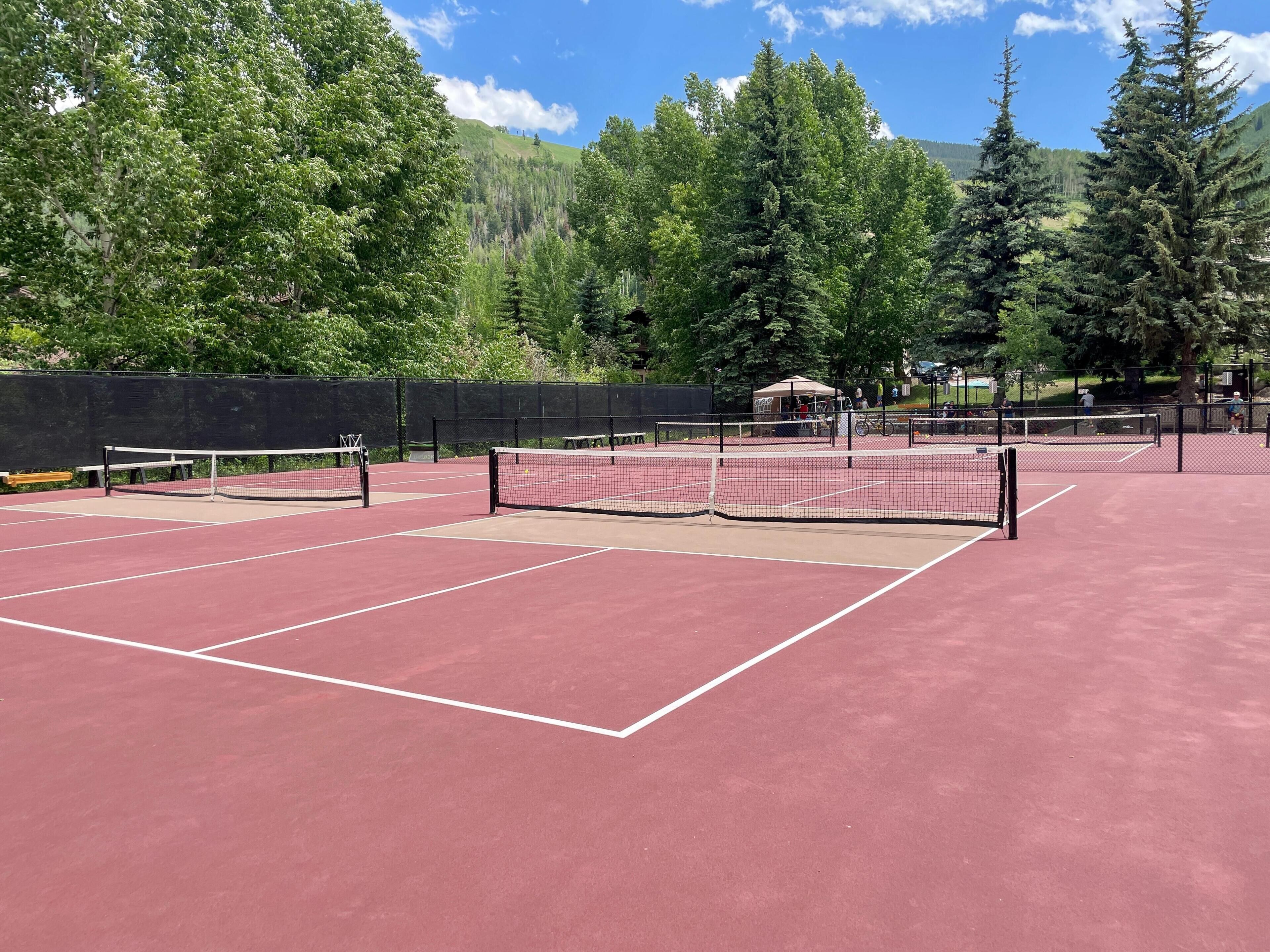Una cancha de tenis con red, rodeada de árboles y una montaña al fondo.