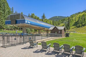 A covered outdoor seating area with Adirondack chairs, a building with a blue and white awning, and a mountainous backdrop. - Vail Trails East 6, 2BD + Loft Condo on East Side Vail Village (Vail)