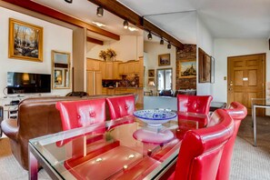 A living room with a glass coffee table, red leather sofas, a TV, and a kitchen in the background. - Vail Trails East 6, 2BD + Loft Condo on East Side Vail Village (Vail)