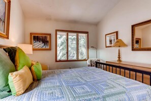 A bedroom with a bed, pillows, a dresser, a lamp, a mirror, and a window with a view of trees. - Vail Trails East 6, 2BD + Loft Condo on East Side Vail Village (Vail)