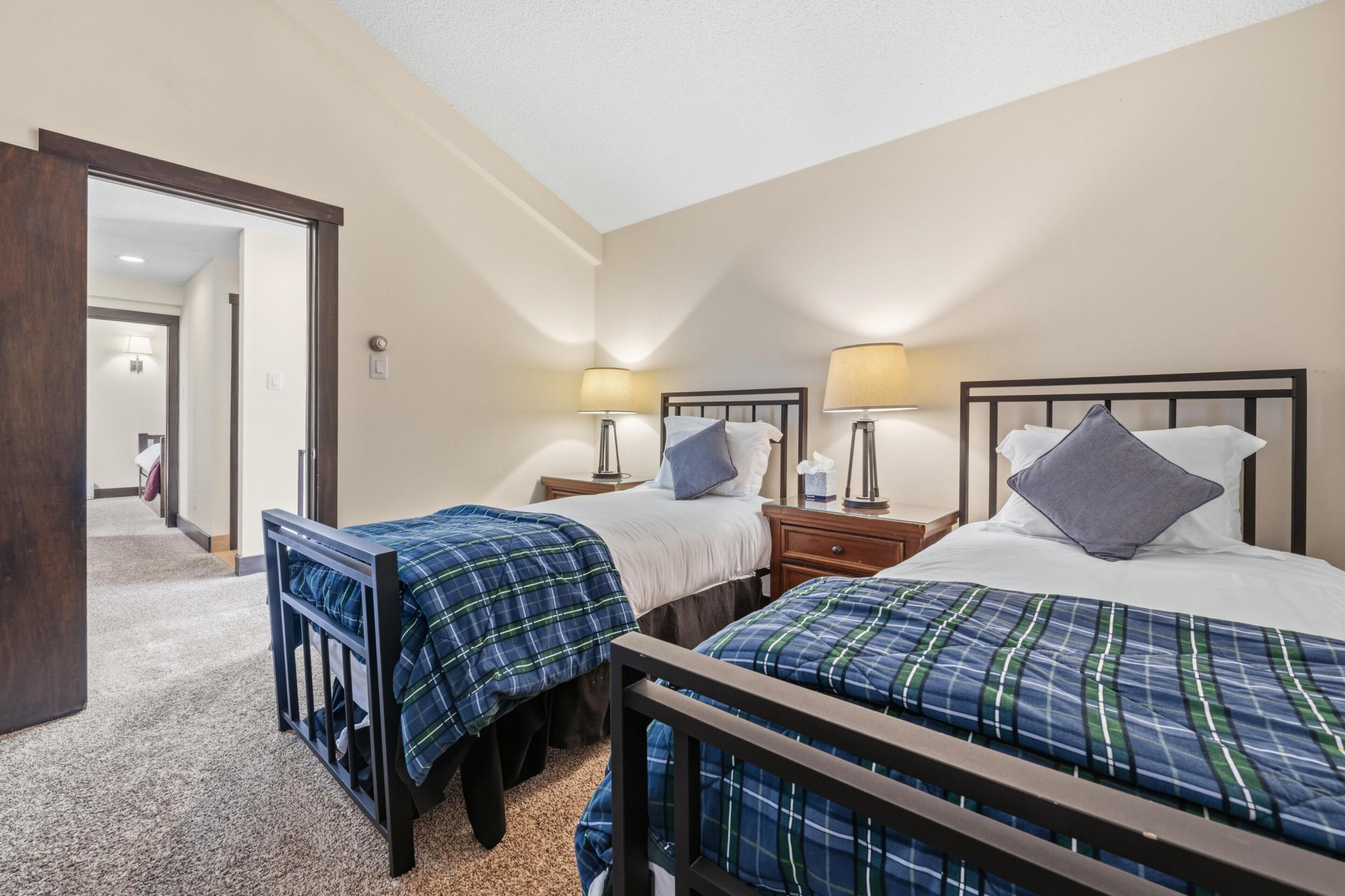 A hotel room with two beds, each with a headboard, bedside tables with lamps, and a carpeted floor.
