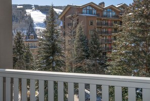 Un hotel de varios pisos con balcones, una torre del reloj y una montaña nevada al fondo.