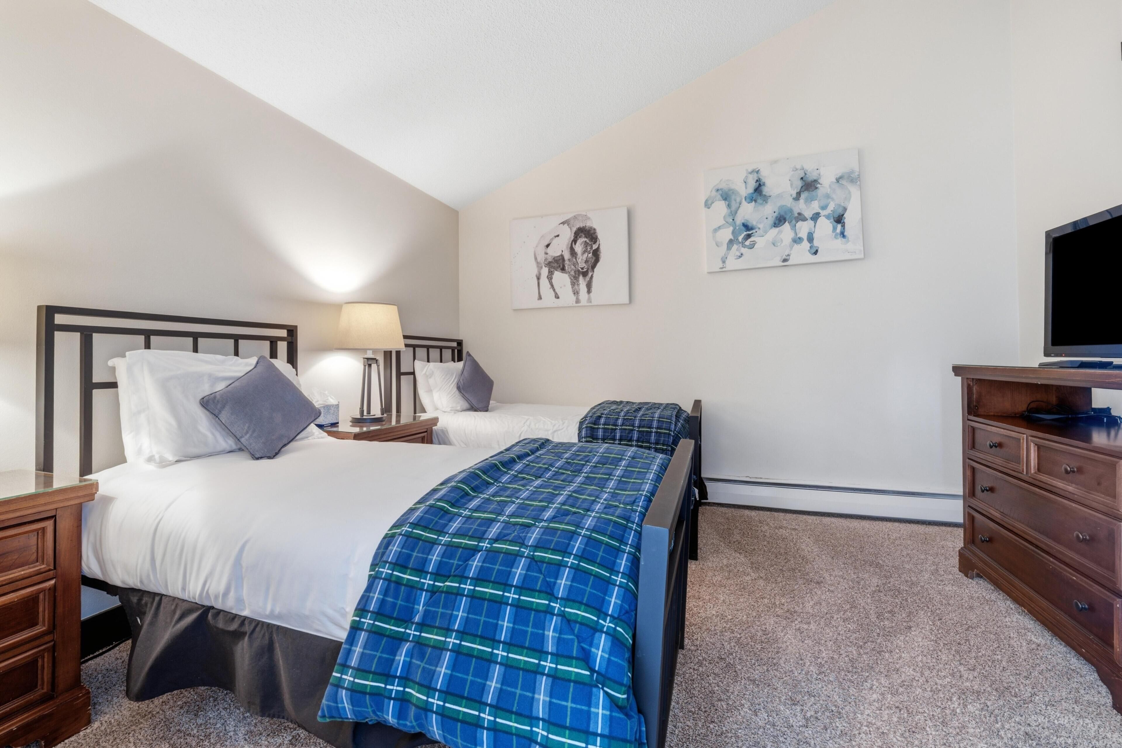 Een hotelkamer met twee bedden, een televisie, een dressoir en kunstwerken aan de muur.