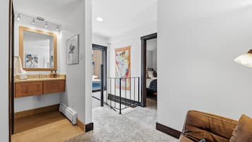 Un interior moderno con piso de madera, un radiador blanco, un baño con tocador de madera y un sofá de cuero marrón.