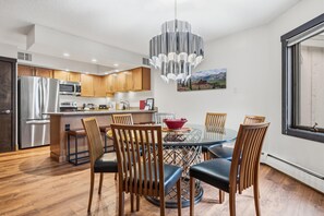 Una cocina moderna con electrodomésticos de acero inoxidable, armarios de madera y un comedor con mesa y sillas de vidrio.