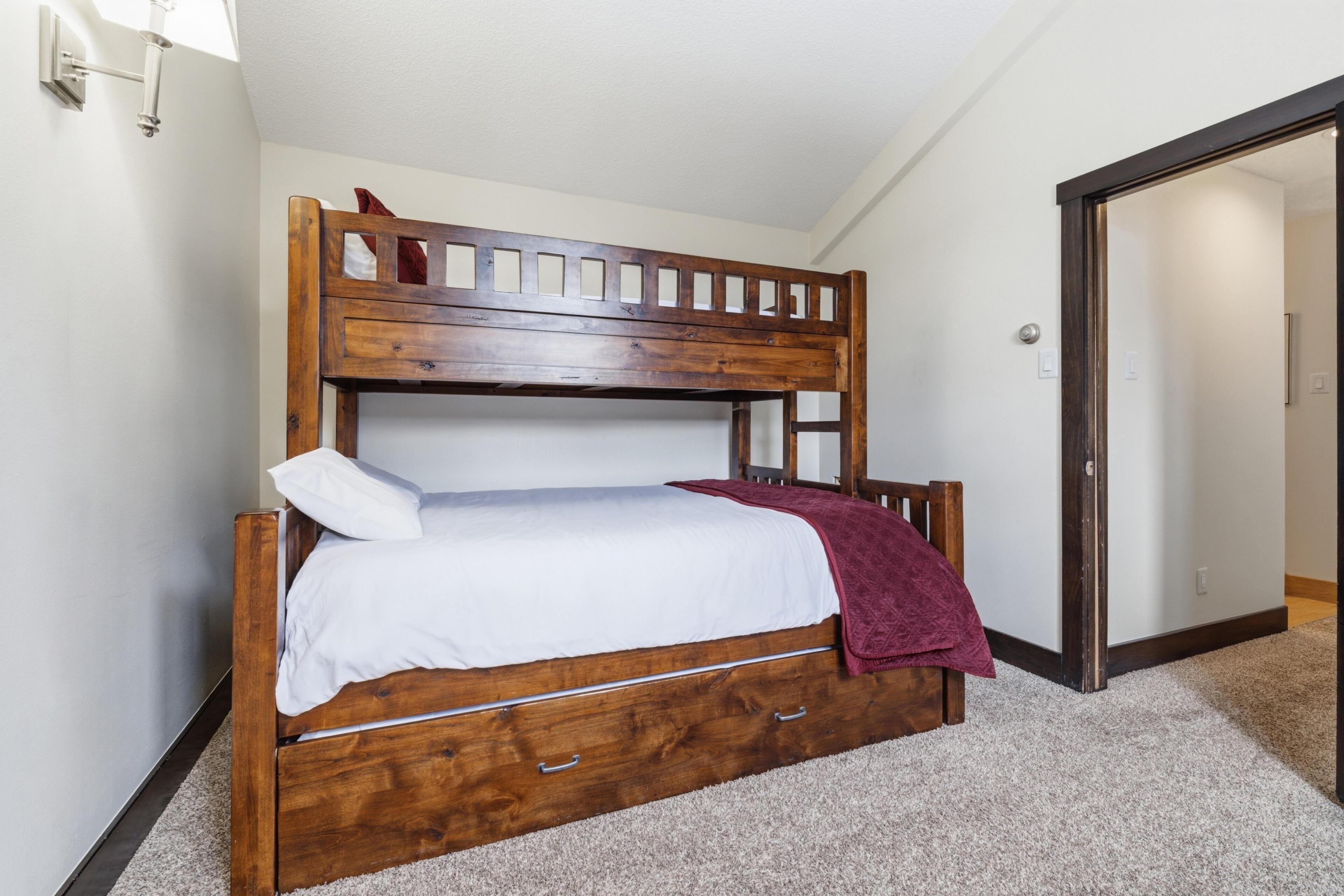 A bunk bed with a wooden frame, white bedding, and a maroon throw blanket.