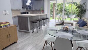 A modern kitchen with a central island, bar stools, a glass dining table with white chairs, and a view of the outdoors. - Apartment in Playa Herradura (Herradura)