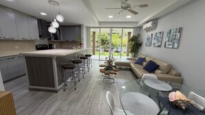 A modern kitchen with a central island, bar stools, a glass dining table, and a ceiling fan. - Apartment in Playa Herradura (Herradura)
