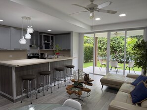 A modern kitchen with a central island, bar stools, and a dining area with a sofa and chairs. - Apartment in Playa Herradura (Herradura)