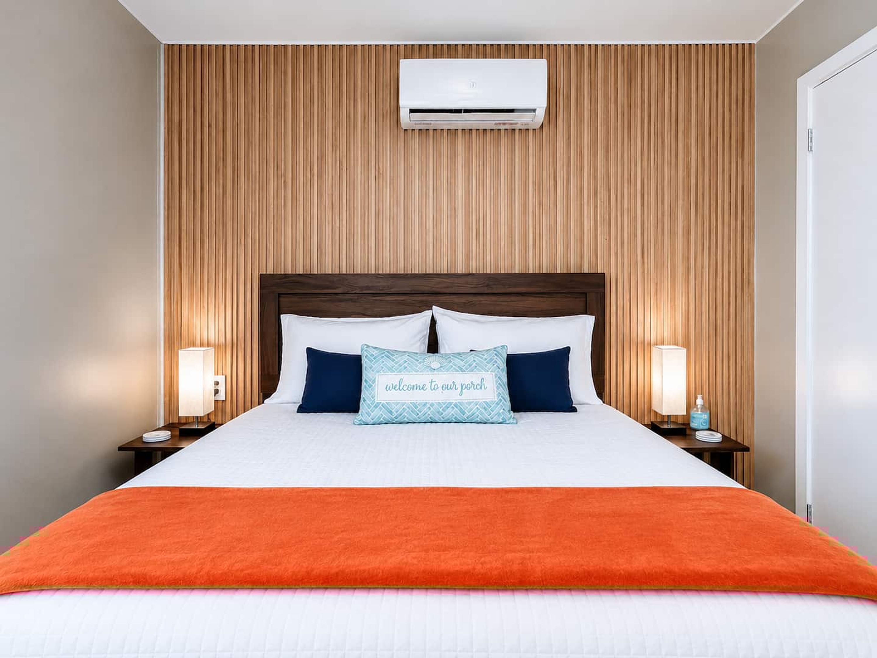 A hotel room with a wooden panel wall, a bed with white bedding, two bedside lamps, and a nightstand with a bottle.