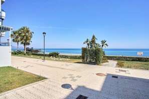 Uma passarela pavimentada com palmeiras, céu azul límpido e vista para o mar.