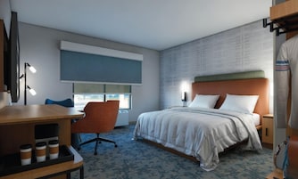 Habitación de hotel con cama, escritorio con silla, ventana y pared con diseño texturizado.